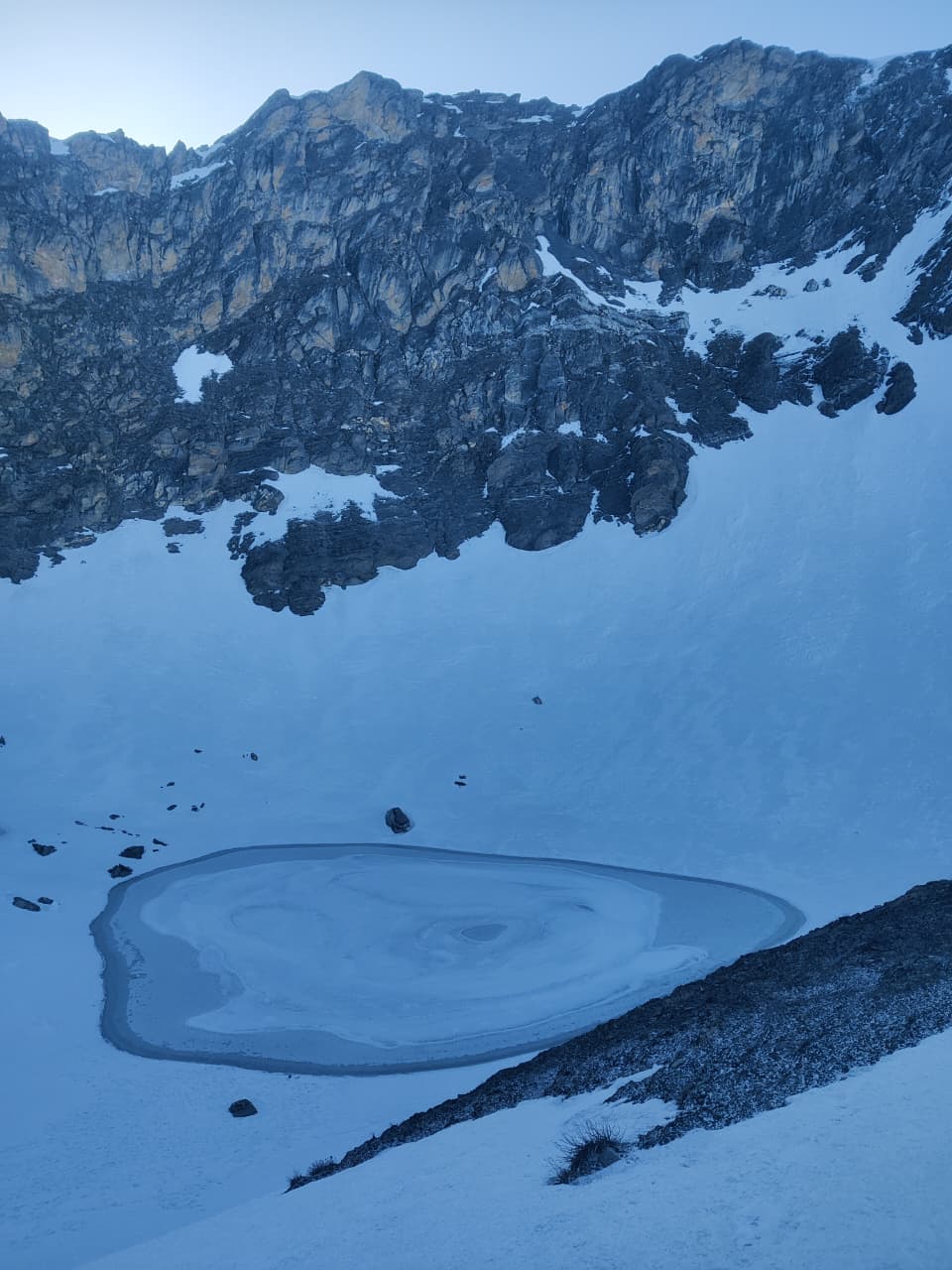 Roopkund's frozen lake resting in shadow while the first sunlight touches the cliffs above